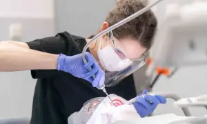 Dentystka w masce i rękawiczkach wykonuje zabieg. Leczenie zębów pod narkozą ryzyko jest minimalizowane przez profesjonalizm.