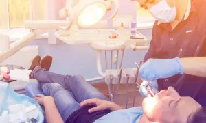 Dentysta w rękawiczkach wykonuje zabieg wyrwania zęba pacjentowi leżącemu na fotelu.