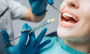 Dentysta podaje znieczulenie powierzchniowe. Pacjentka ma otwarte usta, a stomatolog używa strzykawki i narzędzia.