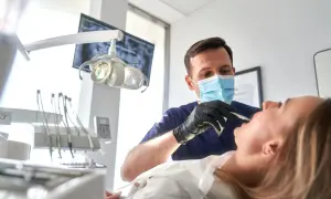 Dentysta w masce wykonuje zabieg szynowania zębów u pacjentki.