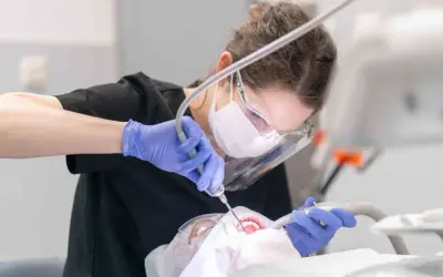 Dentystka w masce i rękawiczkach wykonuje zabieg. Leczenie zębów pod narkozą ryzyko jest minimalizowane przez profesjonalizm.