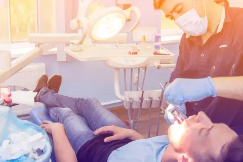 Dentysta w rękawiczkach wykonuje zabieg wyrwania zęba pacjentowi leżącemu na fotelu.
