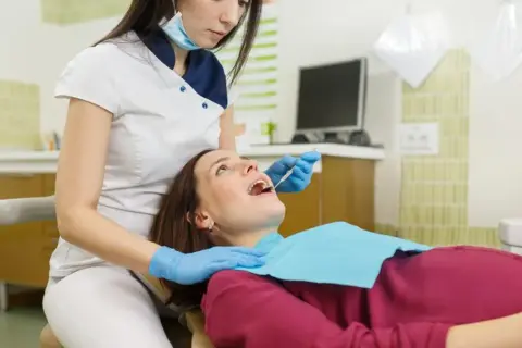Dentystka bada zęby ciężarnej pacjentki. Bezpieczne wybielanie zębów w ciąży jest możliwe po konsultacji.