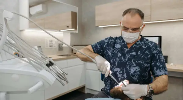 Dentysta w masce i okularach lecząc pacjenta z hiperdoncją zębów na podniebieniu.