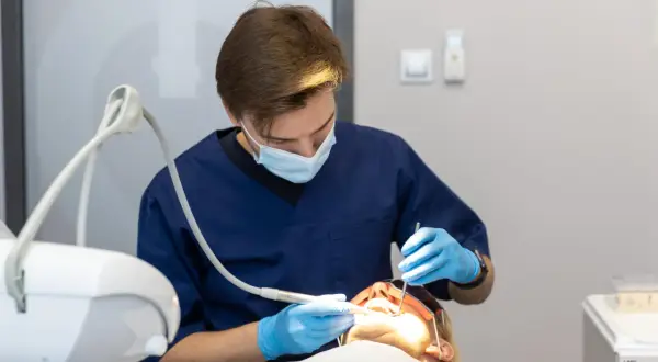 Dentysta w masce i rękawiczkach wykonuje zabieg. Znieczulenie komputerowe przeciwwskazania są ważne dla bezpieczeństwa pacjenta.