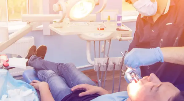 Dentysta w rękawiczkach wykonuje zabieg wyrwania zęba pacjentowi leżącemu na fotelu.