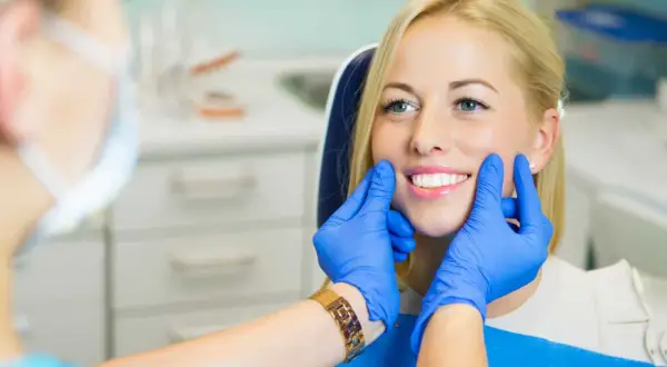 Uśmiechnięta pacjentka z pięknymi zębami, dentysta ocenia estetykę stomatologiczną.