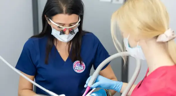 Dentystka w okularach powiększających i asystentka pracują przy pacjencie. Czy znieczulenie u dentysty jest szkodliwe? Nie, jest bezpieczne.