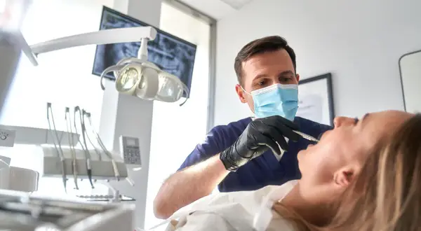 Dentysta w masce wykonuje zabieg szynowania zębów u pacjentki.