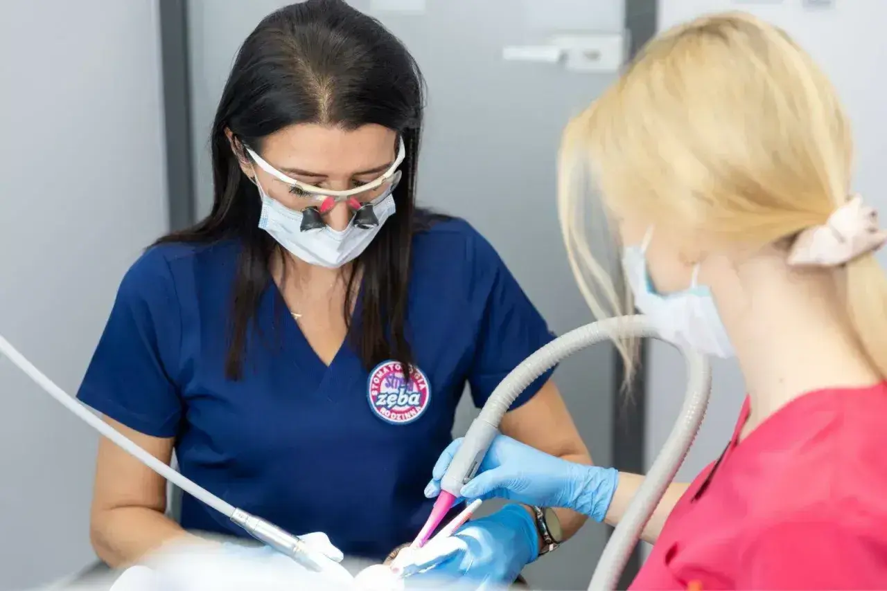 Dentystka w okularach powiększających i asystentka pracują przy pacjencie. Czy znieczulenie u dentysty jest szkodliwe? Nie, jest bezpieczne.