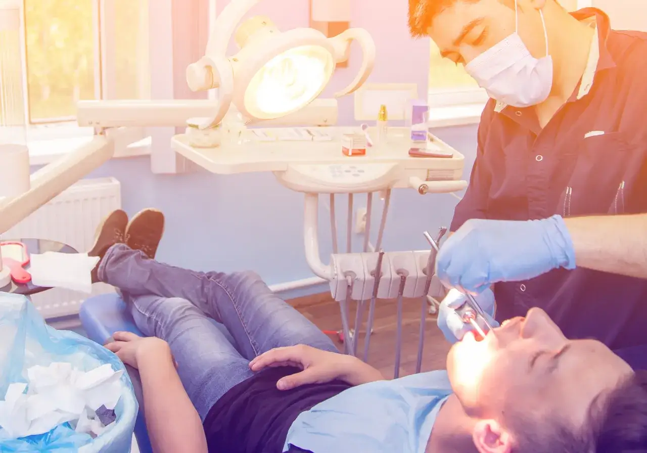 Dentysta w rękawiczkach wykonuje zabieg wyrwania zęba u pacjenta leżącego na fotelu.