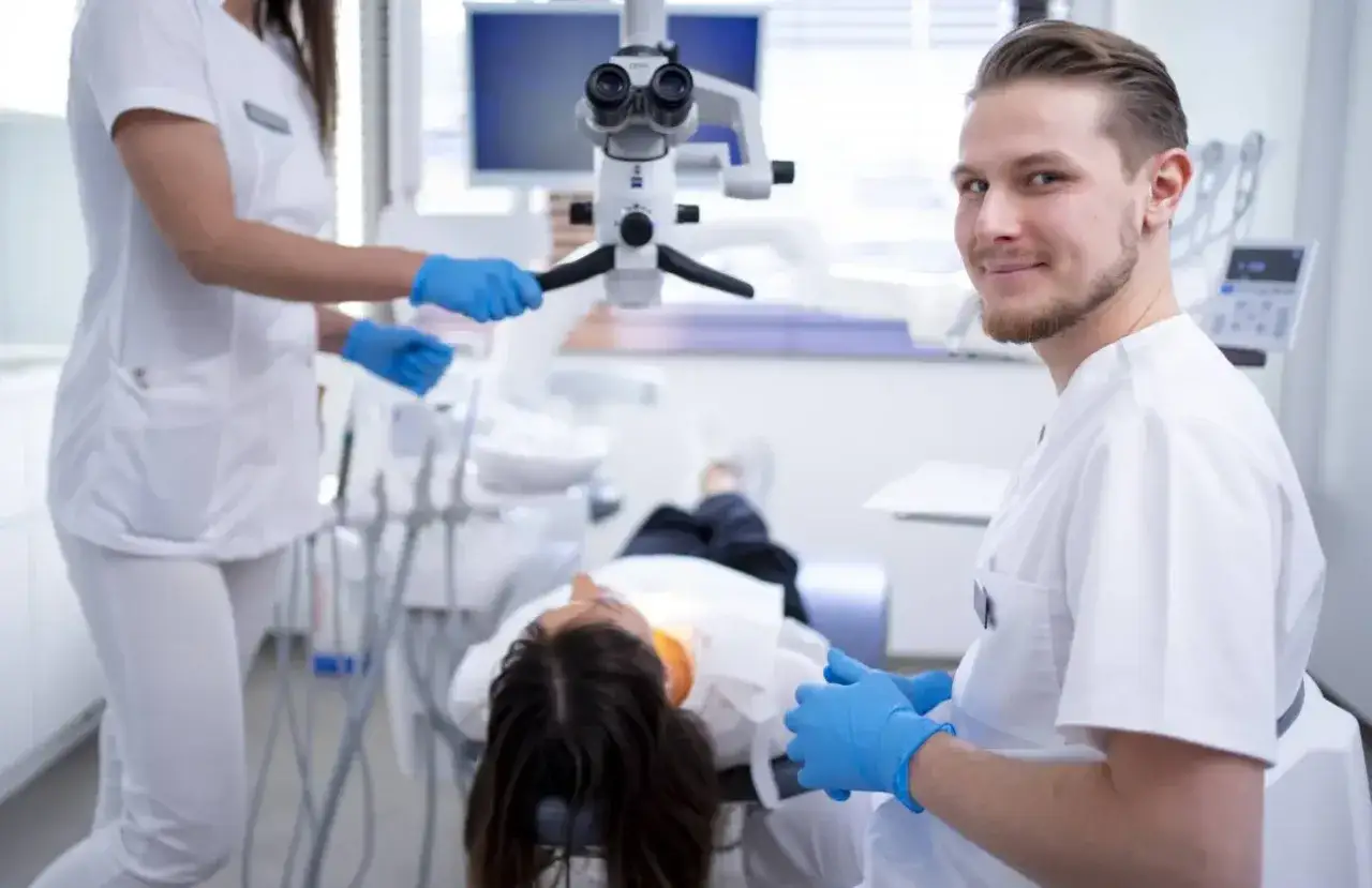Uśmiechnięty dentysta w gabinecie. Pacjentka leży na fotelu. Czy znieczulenie u dentysty jest szkodliwe? Zazwyczaj nie, jest bezpieczne.