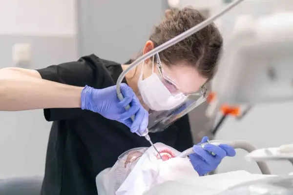 Dentystka w masce i rękawiczkach wykonuje zabieg. Leczenie zębów pod narkozą ryzyko jest minimalizowane przez profesjonalizm.