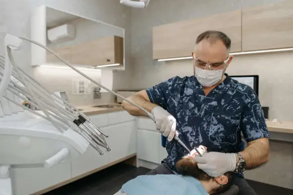 Dentysta w masce i okularach lecząc pacjenta z hiperdoncją zębów na podniebieniu.