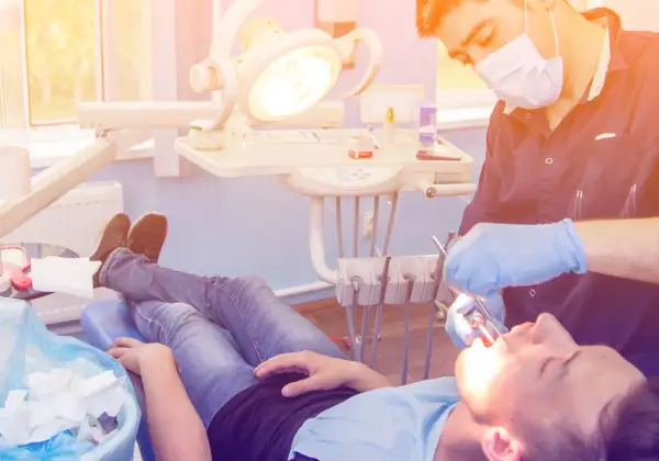 Dentysta w rękawiczkach wykonuje zabieg wyrwania zęba pacjentowi leżącemu na fotelu.