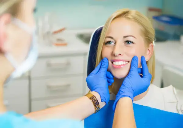 Uśmiechnięta pacjentka z pięknymi zębami, dentysta ocenia estetykę stomatologiczną.